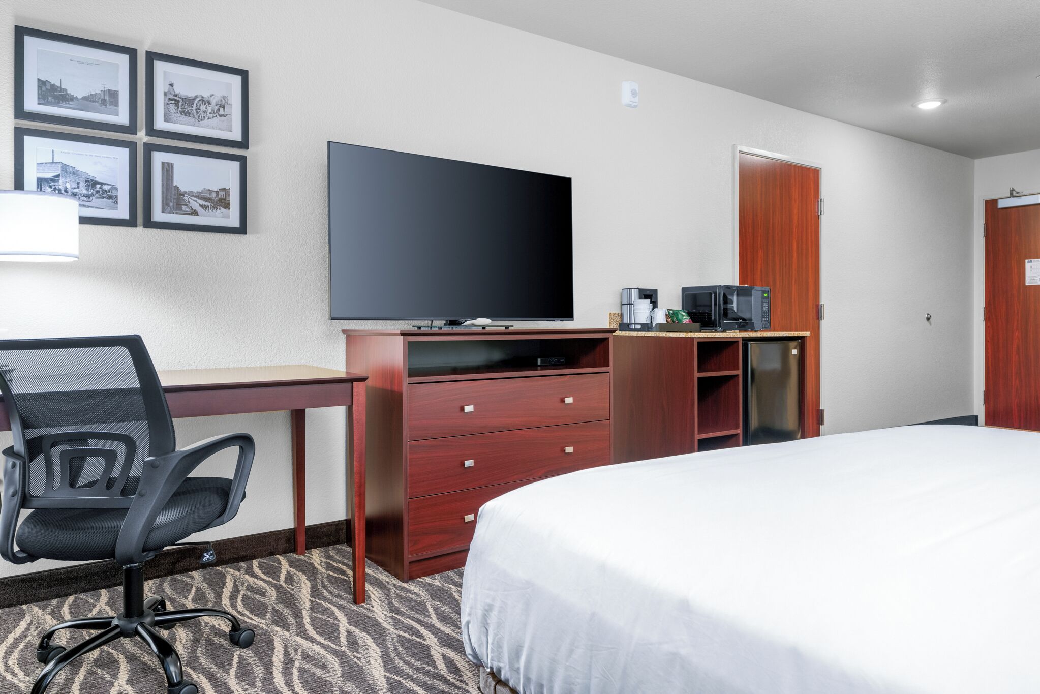 A hotel room with a bed, a desk with a chair, a television, a microwave, and a coffee maker.