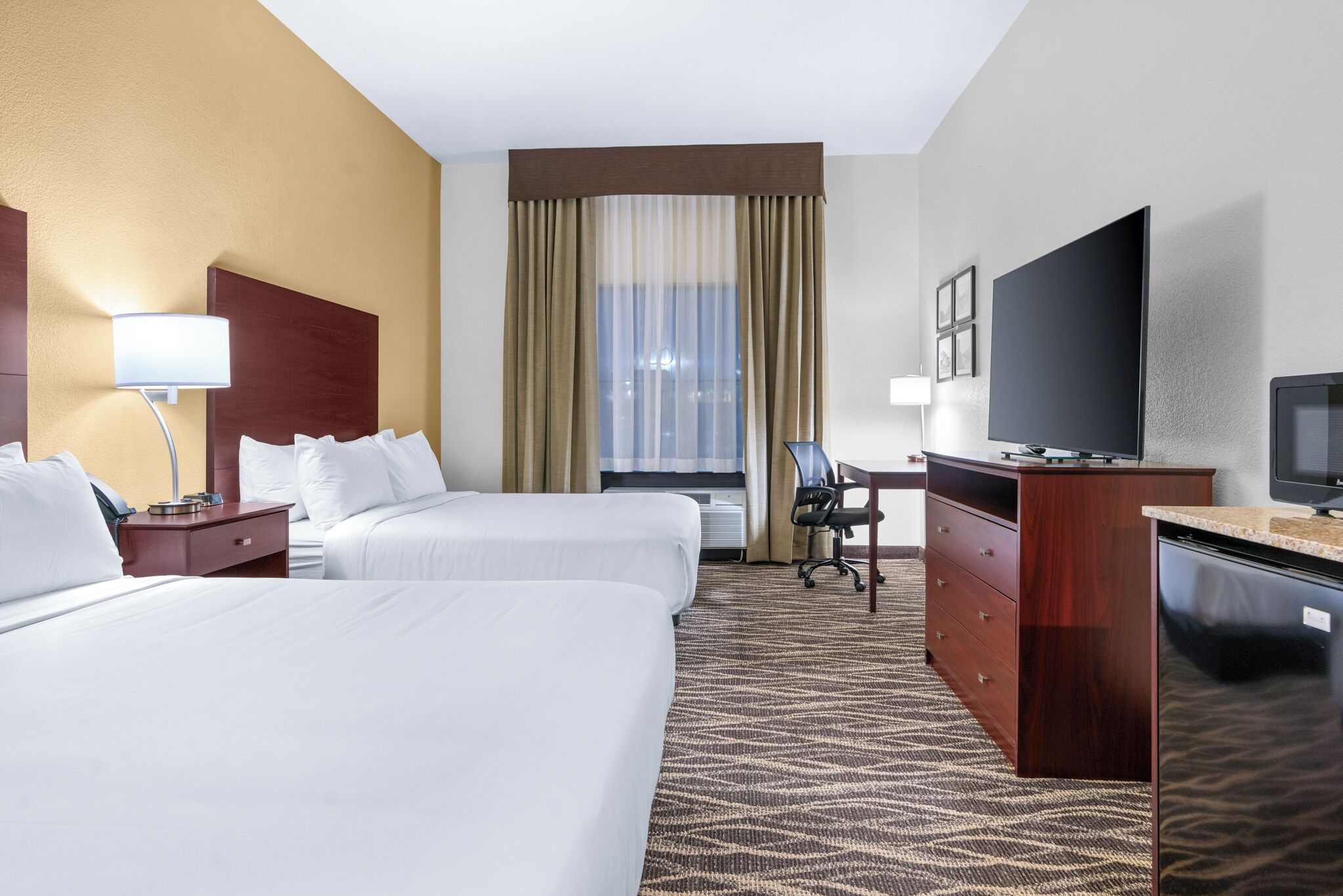 A hotel room with two beds, a desk, a television, and a minibar.