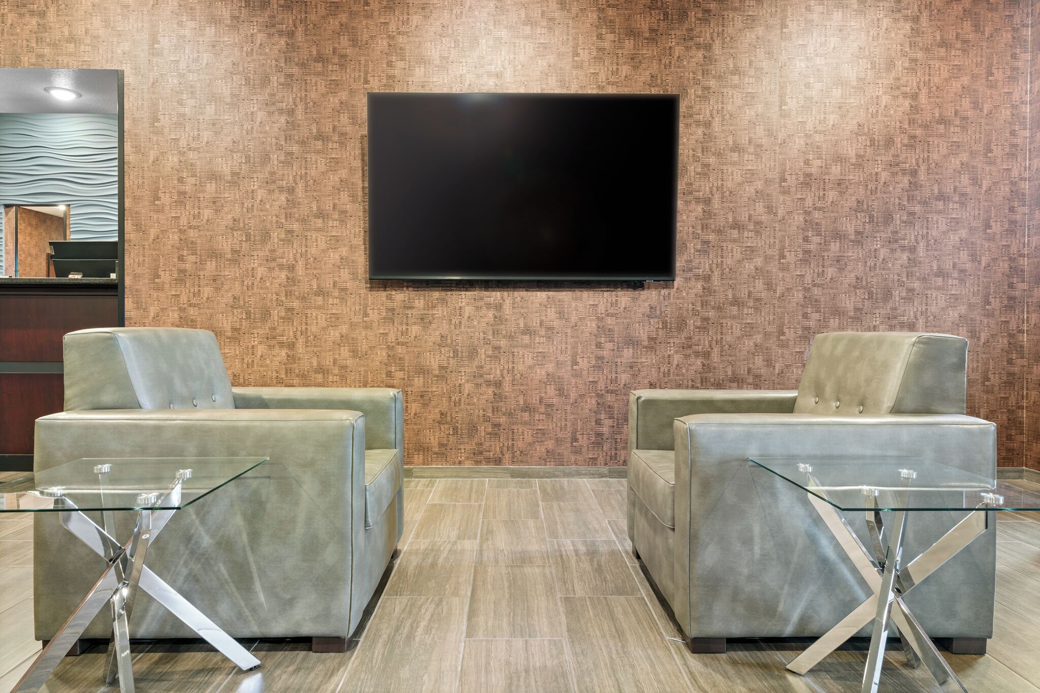 En entréhall med två bekväma sittgrupper, en platt-TV som är monterad på väggen och en receptionsdisk med en mönstrad bakgrund.