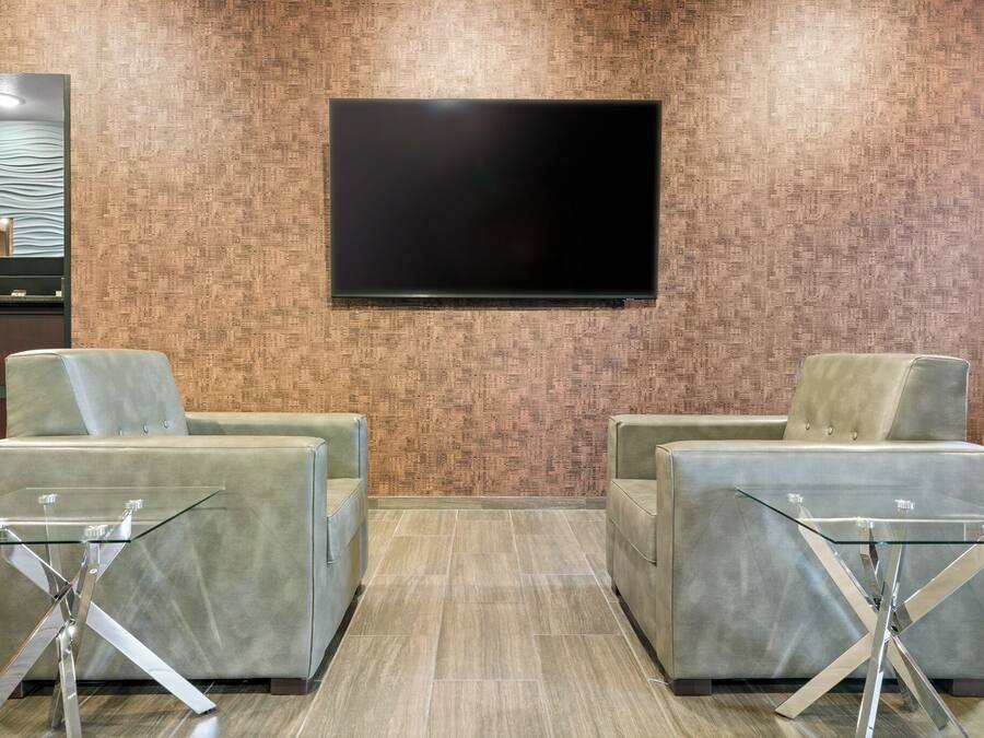 En entréhall med två bekväma sittgrupper, en platt-TV som är monterad på väggen och en receptionsdisk med en mönstrad bakgrund.