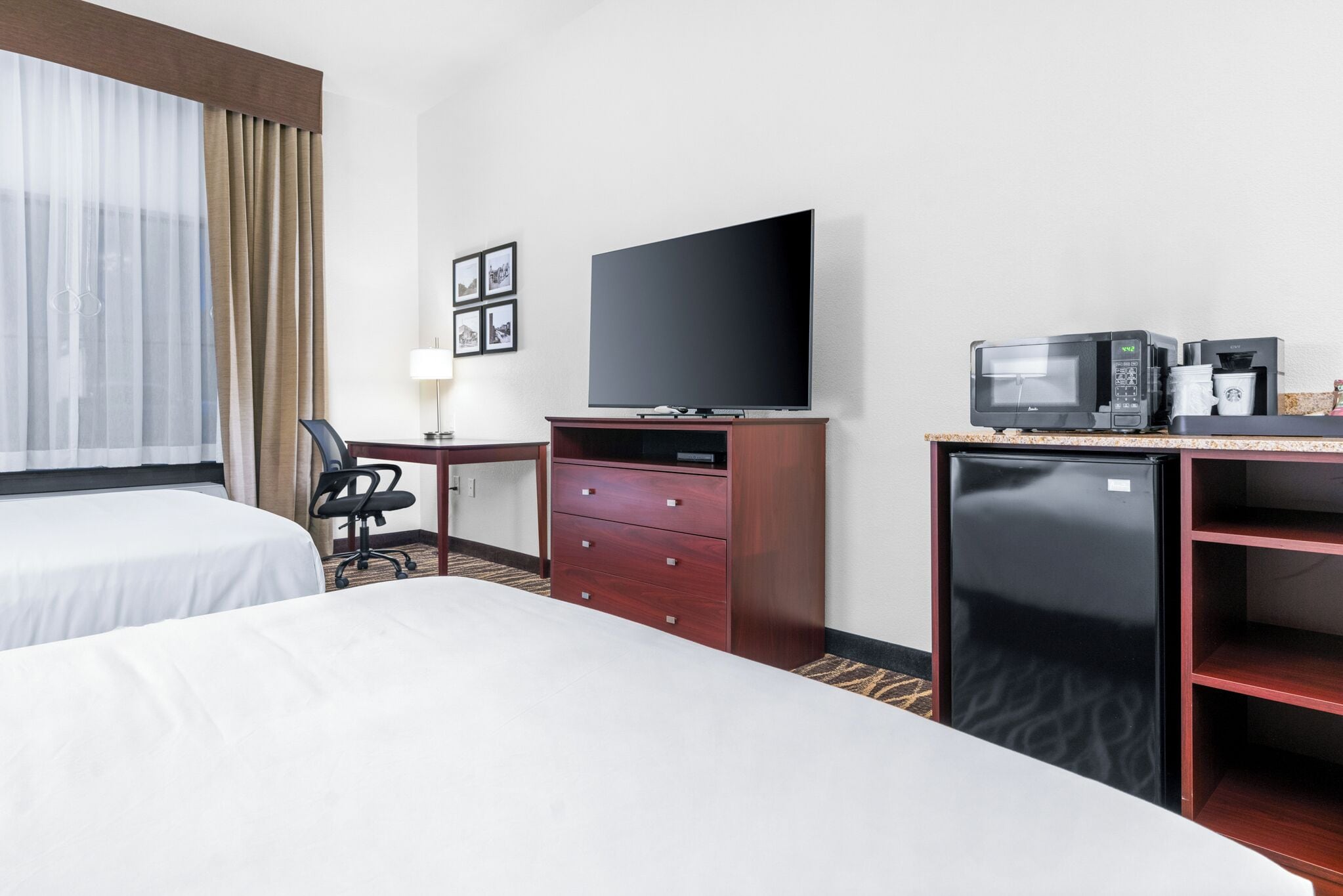 Habitación de hotel con dos camas, televisión, mini refrigerador, microondas y cafetera.