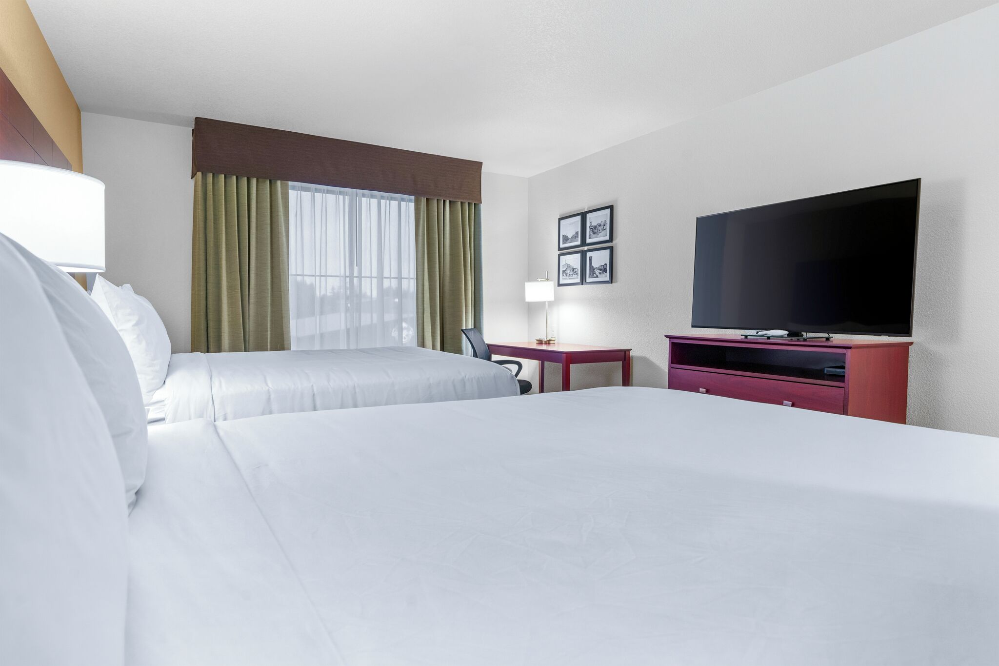 Ein Hotelzimmer mit zwei Betten, einem Schreibtisch, einem Fernseher und einem Fenster mit Vorhängen.