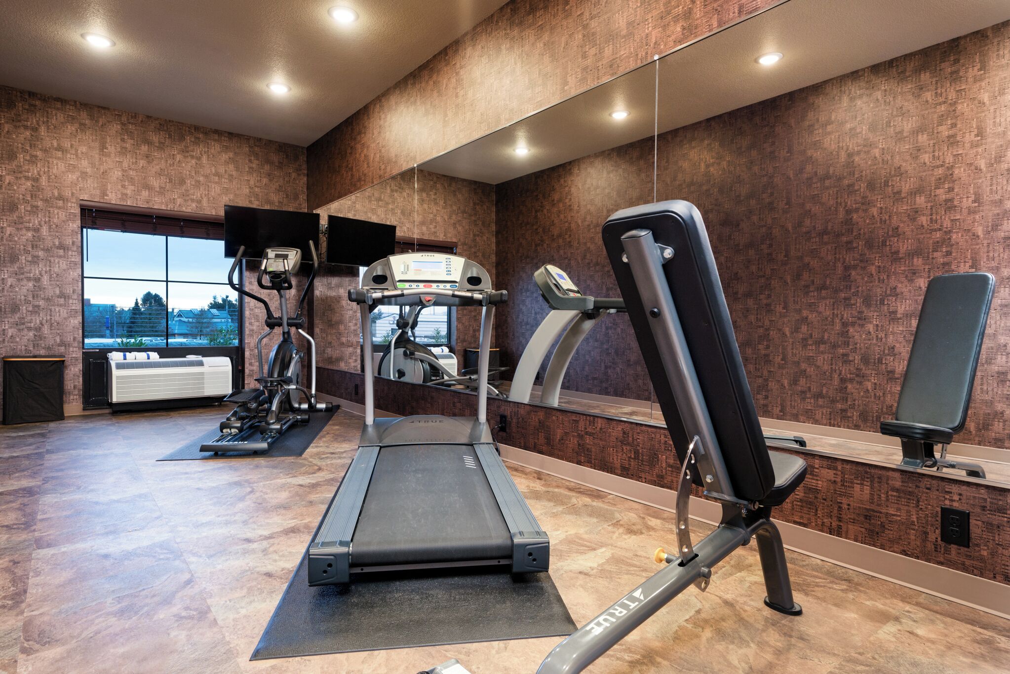 A gym with a treadmill, elliptical, and weight bench.
