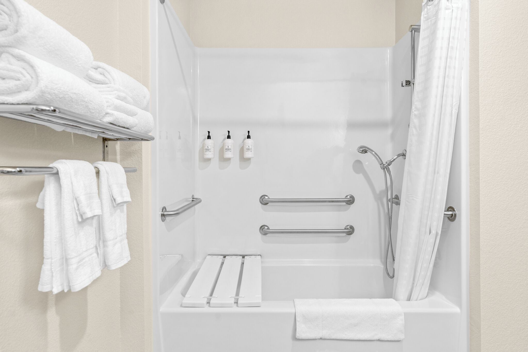 A modern shower area with a bathtub, grab bars, and a towel rack with folded towels.