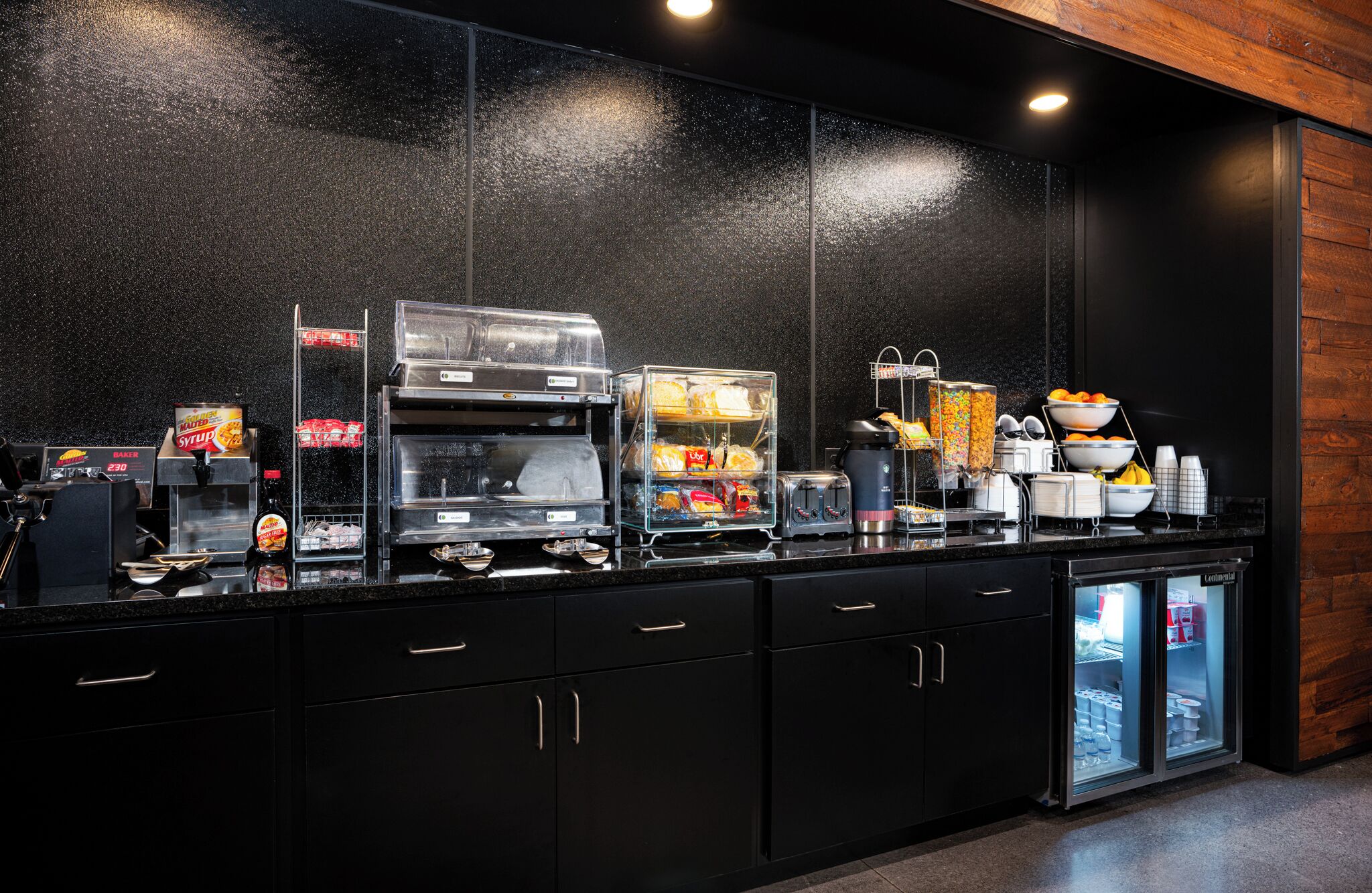 Un área de cocina moderna con estación de café, exhibición de panadería y refrigerador.