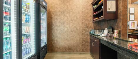 A kitchen with a granite countertop, a microwave, and a refrigerator stocked with beverages.