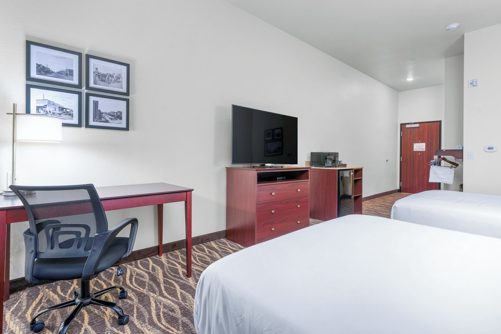 Quarto de hotel com escrivaninha, cadeira, televisão e duas camas.