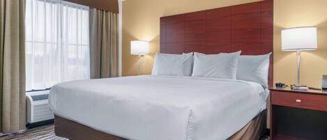 Habitación de hotel con una cama grande, dos lámparas de noche, un cabecero de madera y una ventana con cortinas.