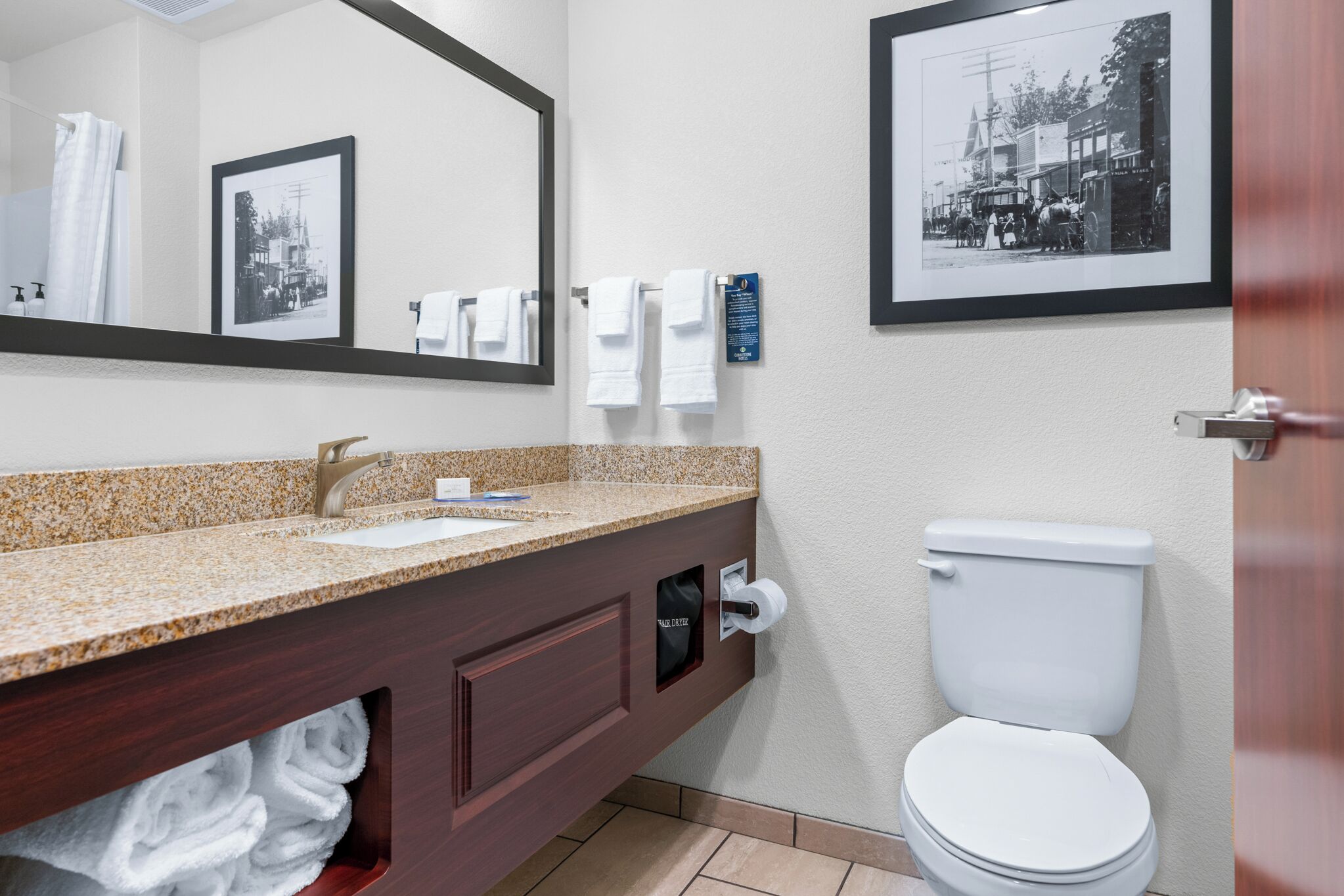 A bathroom with a granite countertop sink, a mirror, a toilet, and two framed pictures on the wall.