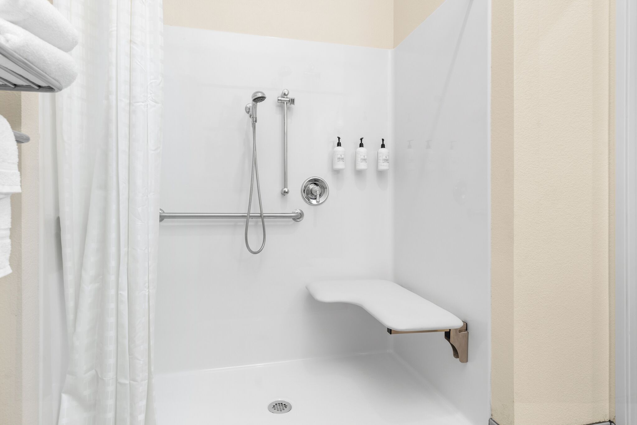 A shower area with a grab bar, a showerhead, and a shelf with toiletries.