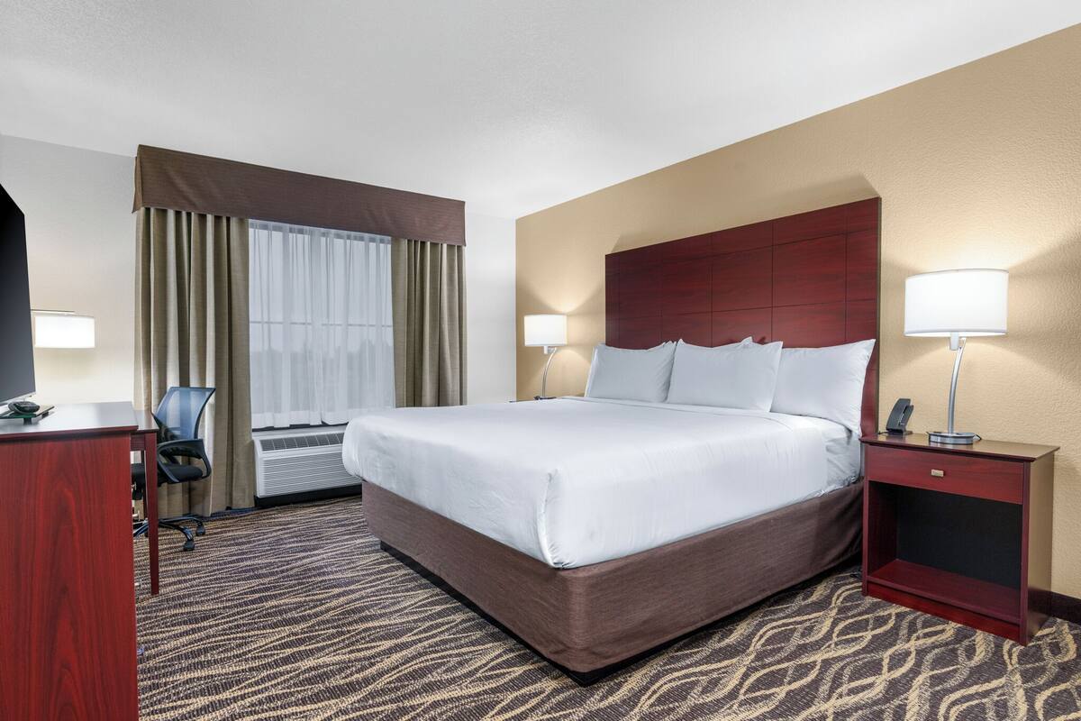 A hotel room with a large bed, a desk, a chair, a lamp, and a window with curtains.