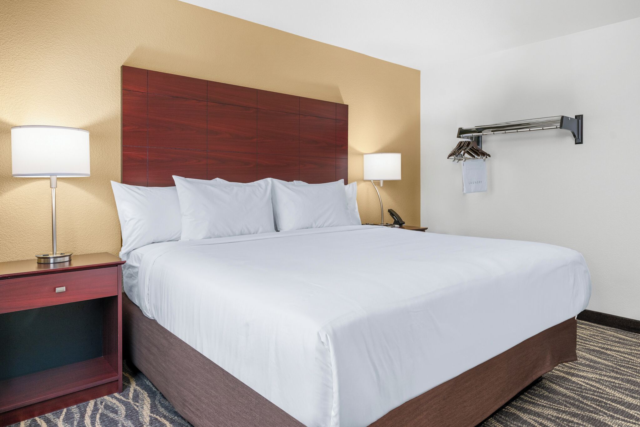A hotel room with a large bed, two bedside tables, a wooden headboard, and a wall-mounted towel rack.
