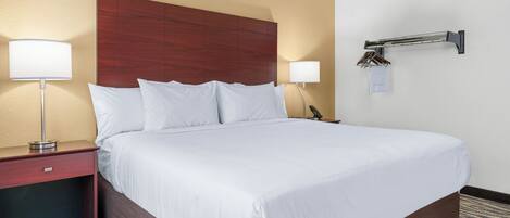 A hotel room with a large bed, two bedside tables, a wooden headboard, and a wall-mounted towel rack.