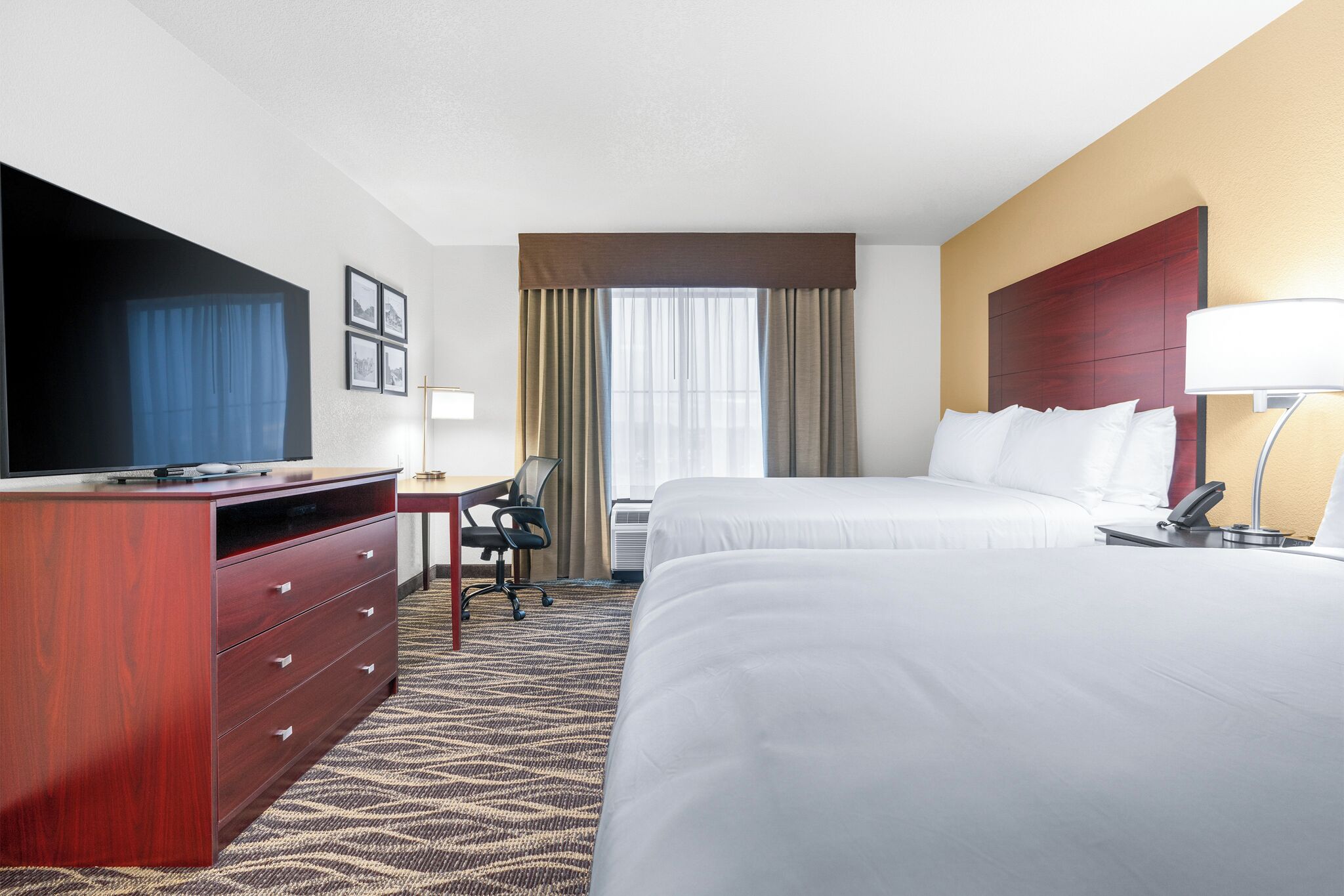 A hotel room with a bed, a desk, a television, and a dresser.