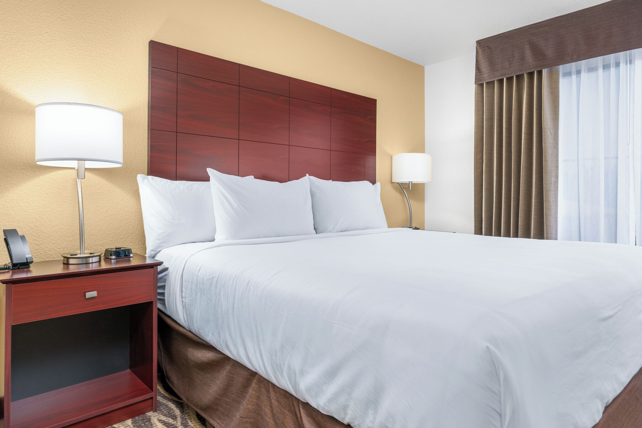 Habitación de hotel con una cama grande, dos mesitas de noche, cabecera de madera y una ventana con cortinas.