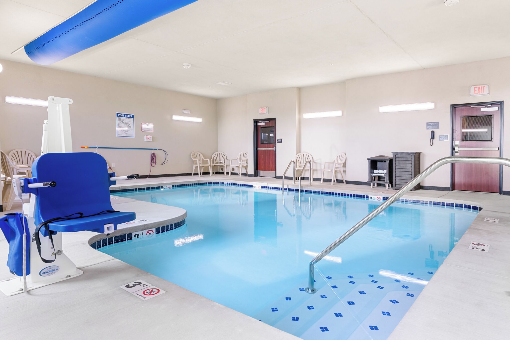 Una piscina con azulejos azules, una silla azul y una silla para socorristas.