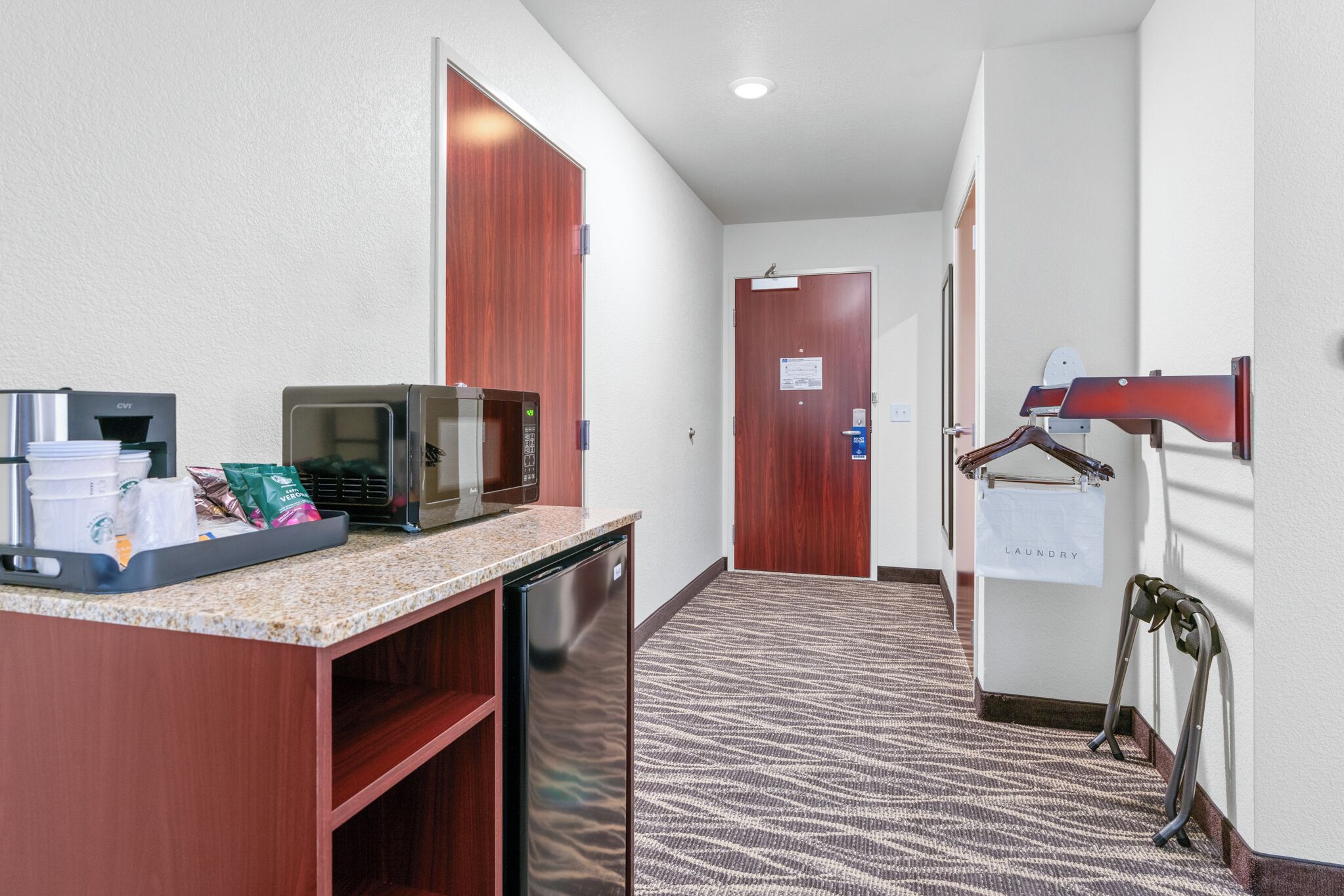 Een hotellobby met een kitchenette, een magnetron, een koffieapparaat en een bord met wassymbolen.