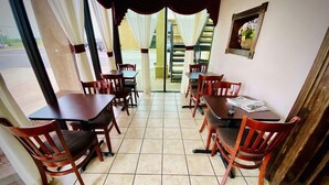 A dining area with wooden tables and chairs, a tiled floor, and a view through a glass door to an outdoor area. - Super 8 By Wyndham Shawnee (Shawnee)
