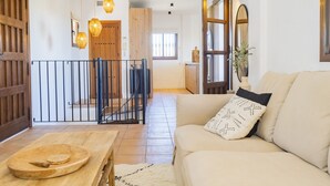 A spacious living area with a wooden dining table, a beige sofa with patterned cushions, and a staircase leading to an upper floor. - Cubo's Casa Rural Pulpito / air conditioning / free wifi / private pool (Coín)