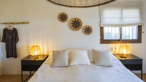 A bedroom with a bed, two bedside tables with lamps, a window with blinds, a wall-mounted shelf with a coat, and decorative wall art. - Cubo's Casa Rural Pulpito / air conditioning / free wifi / private pool (Coín)