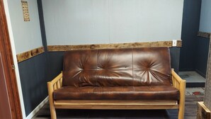 Un canapé en cuir marron, doté de pieds en bois, se trouve dans une pièce dont le sol est recouvert de parquet foncé et le plafond est blanc.