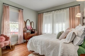 A bedroom with a large bed, a dresser, a vanity with mirrors, and a chair.