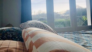 A bedroom with a large window, a bed with patterned bedding, and a wall-mounted decorative item. - Jolie Maison Familiale sur la ria à Saint-cado (Belz)