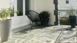 A stone-tiled patio with a black chair and two potted plants. - Jolie Maison Familiale sur la ria à Saint-cado (Belz)