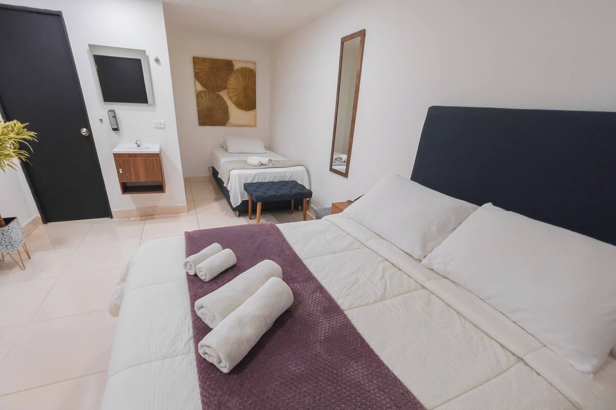 Ein Hotelzimmer mit einem Bett, einem kleinen Schreibtisch, einem Spiegel, einem an der Wand befestigten Fernseher und einem Badezimmer mit Waschbecken und Toilette.