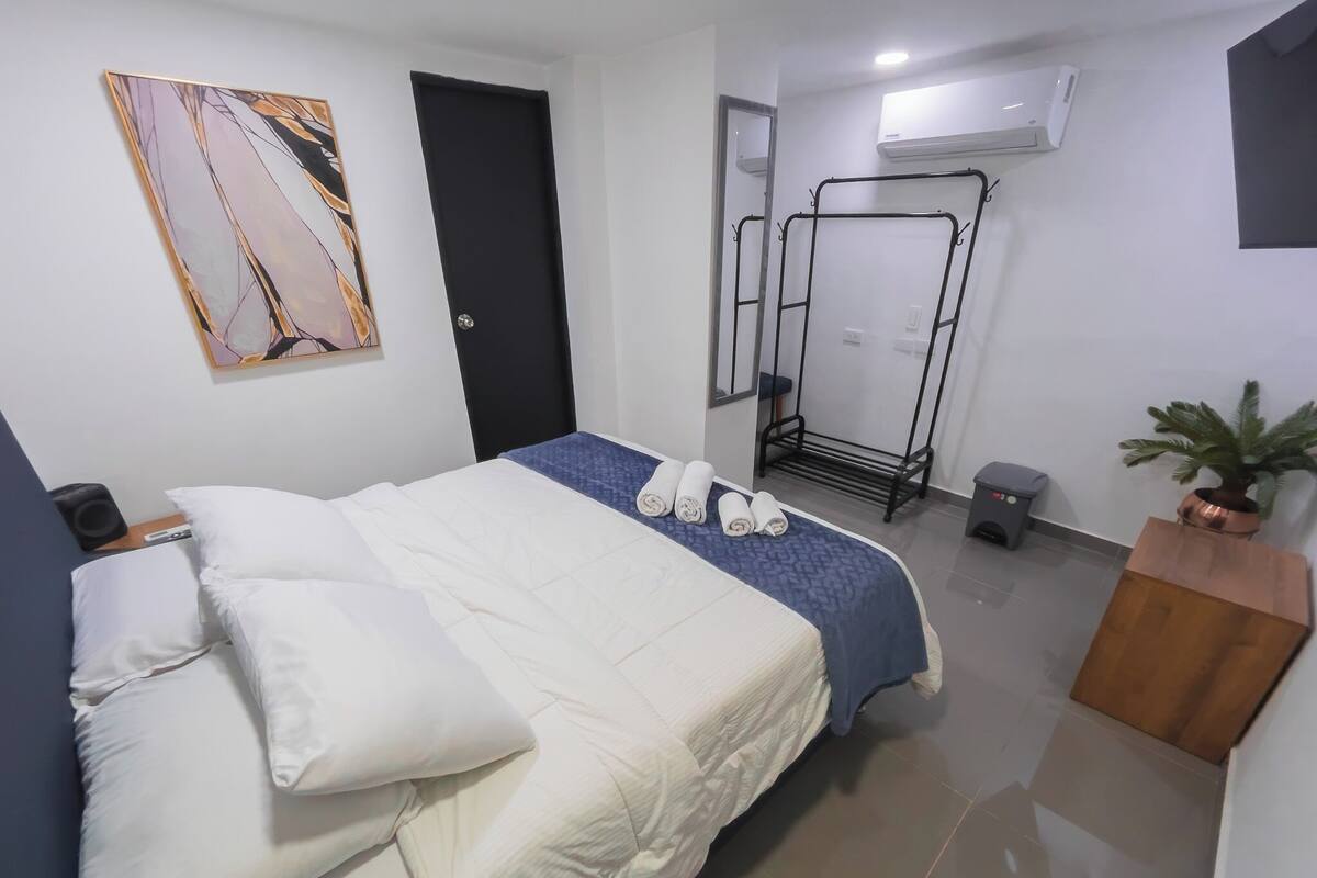 Ein Hotelzimmer mit Bett, Kissen, Handtuchhalter, Zimmerpflanze und Klimaanlage.