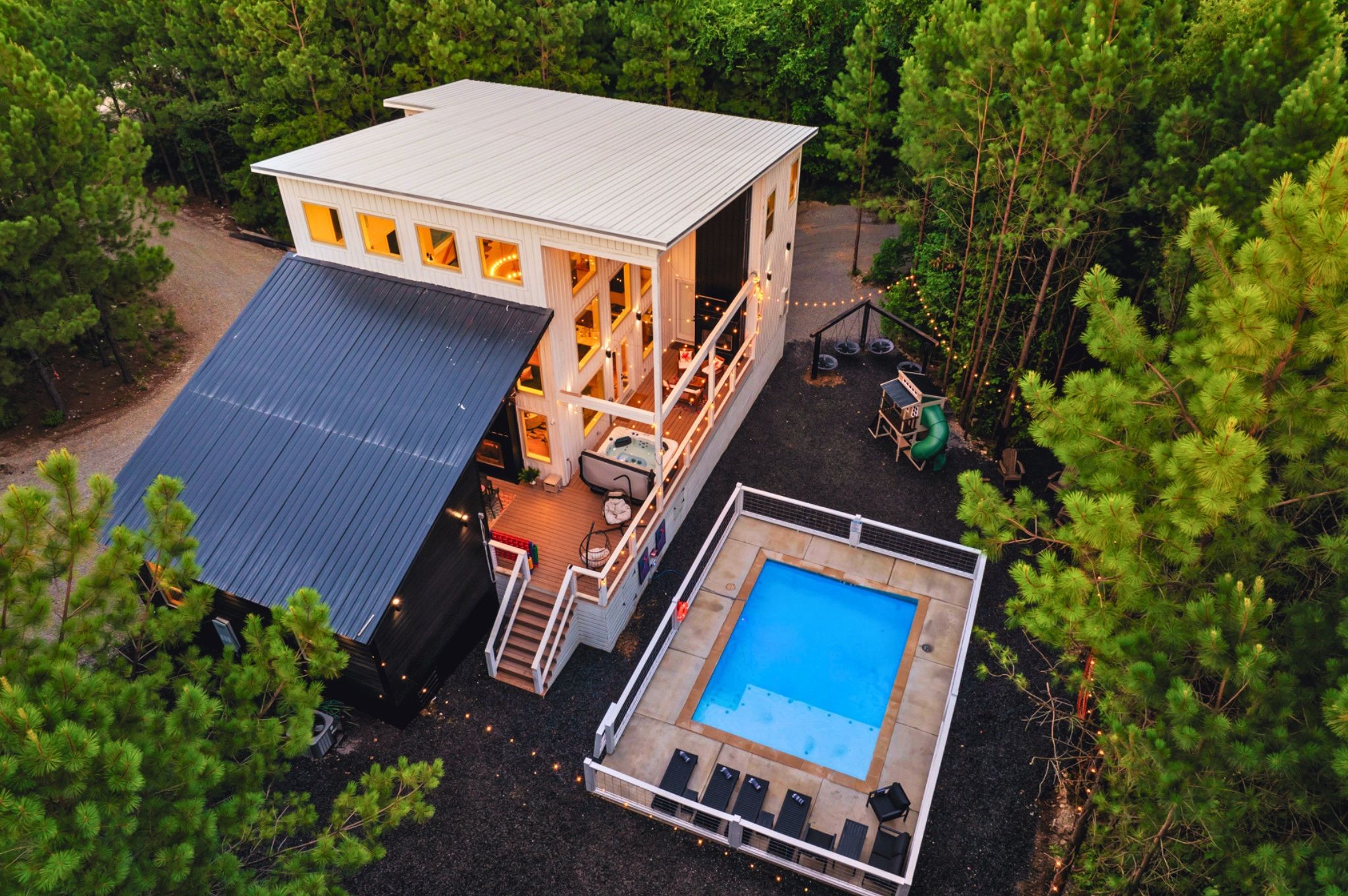 A two-story house with a pool and outdoor seating area surrounded by trees.