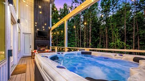 An outdoor hot tub area with a wooden deck, a fireplace, and string lights. - Luxury 3BR in ❤️ of Hochatown! Heated Pool, Playset, Games (Broken Bow)