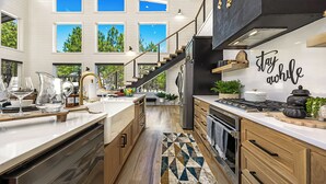 A modern kitchen with a central island, stainless steel appliances, and a staircase leading to an upper level. - Luxury 3BR in ❤️ of Hochatown! Heated Pool, Playset, Games (Broken Bow)
