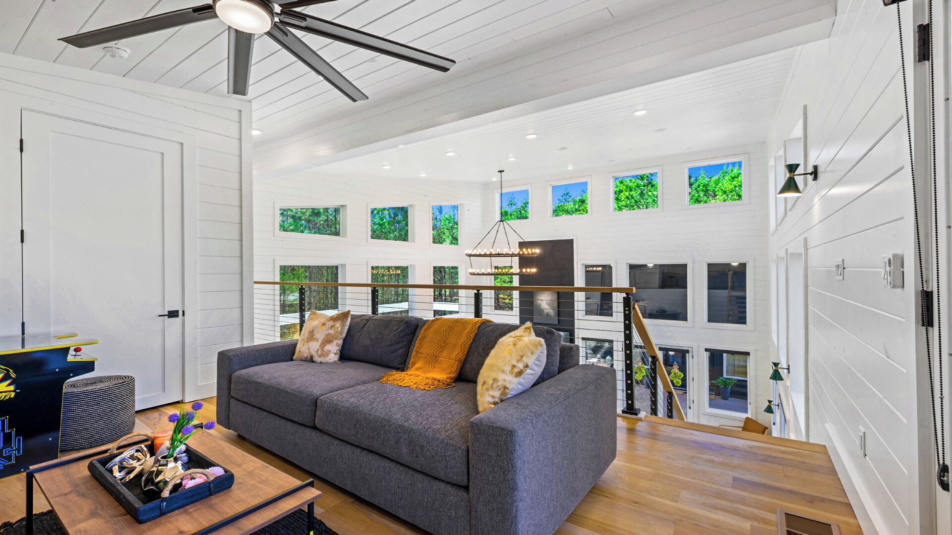 Ein modernes Wohnzimmer mit grauem Sofa, Holzböden und Deckenventilator.