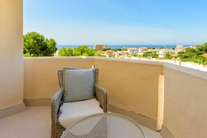 A balcony with a wicker chair and a round table, overlooking a coastal town with buildings and greenery. - Zeus | Cosy Apartment with Stunning Sea Views & Pool in Riviera del Sol (Mijas Costa)