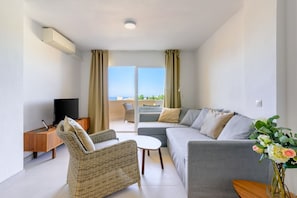 A modern living room with a sofa, a wicker chair, a small table, and a TV on a wooden stand. - Zeus | Cosy Apartment with Stunning Sea Views & Pool in Riviera del Sol (Mijas Costa)