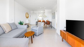 A modern living room with a sofa, a wicker chair, a wooden TV stand, and a dining area with a table and chairs.
