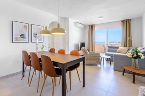 A modern living room with a dining area, a sofa, a TV, and a view of the sea. - Zeus | Cosy Apartment with Stunning Sea Views & Pool in Riviera del Sol (Mijas Costa)