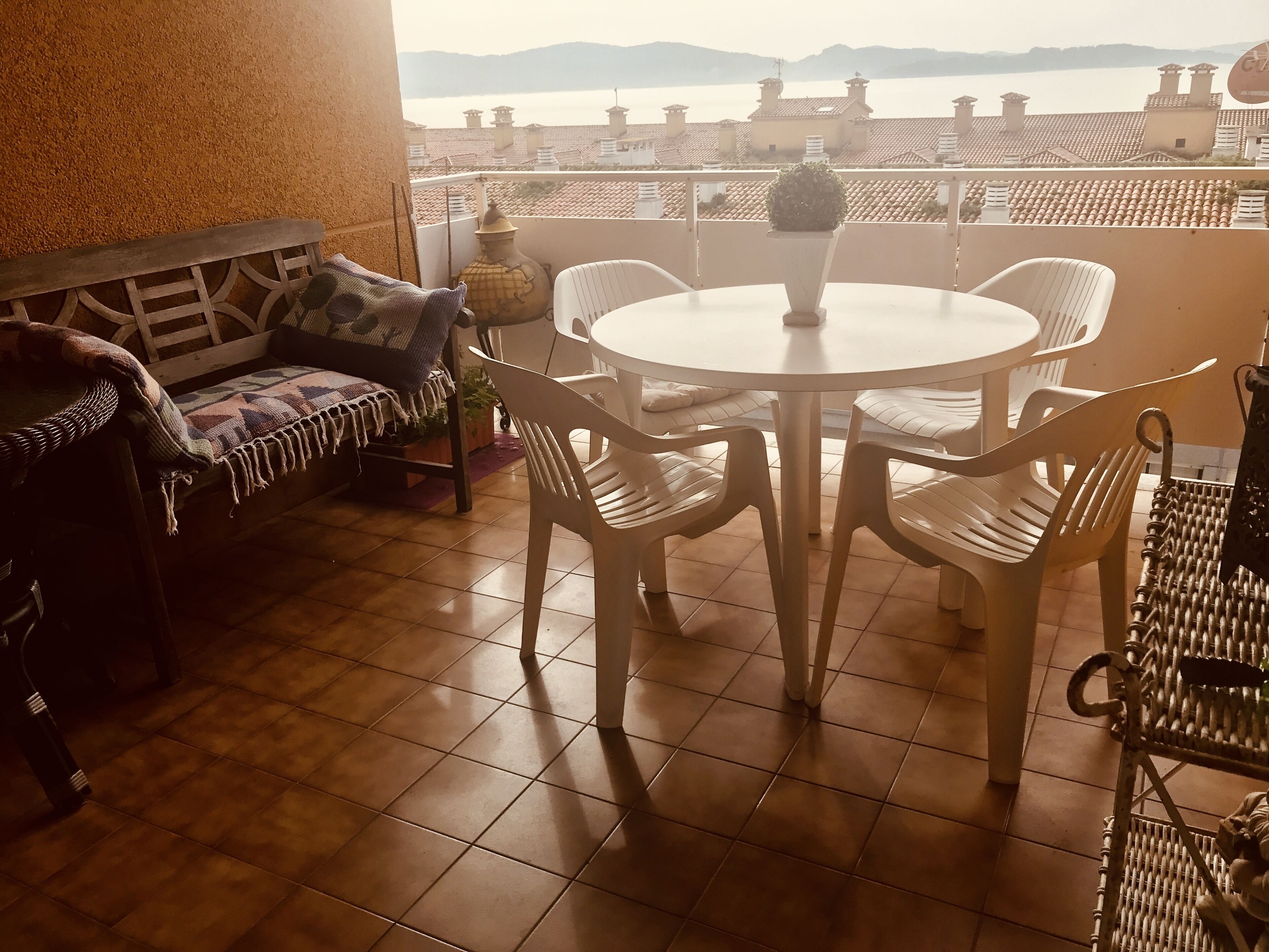 Ein Balkon mit rundem Tisch und Stühlen, einer Couch und Blick auf Gebäude und Wasser.