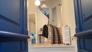 A staircase with white steps and blue walls, leading to a landing with a radiator and a table with a vase of flowers.