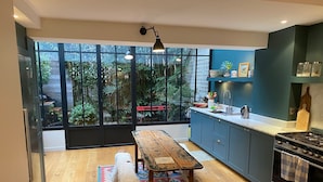 A modern kitchen with a large window, wooden flooring, a dining table, and a stove.