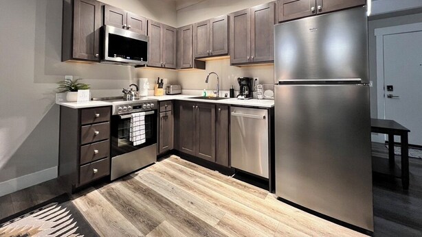 Una cocina moderna con armarios oscuros, electrodomésticos de acero inoxidable y suelo de madera.