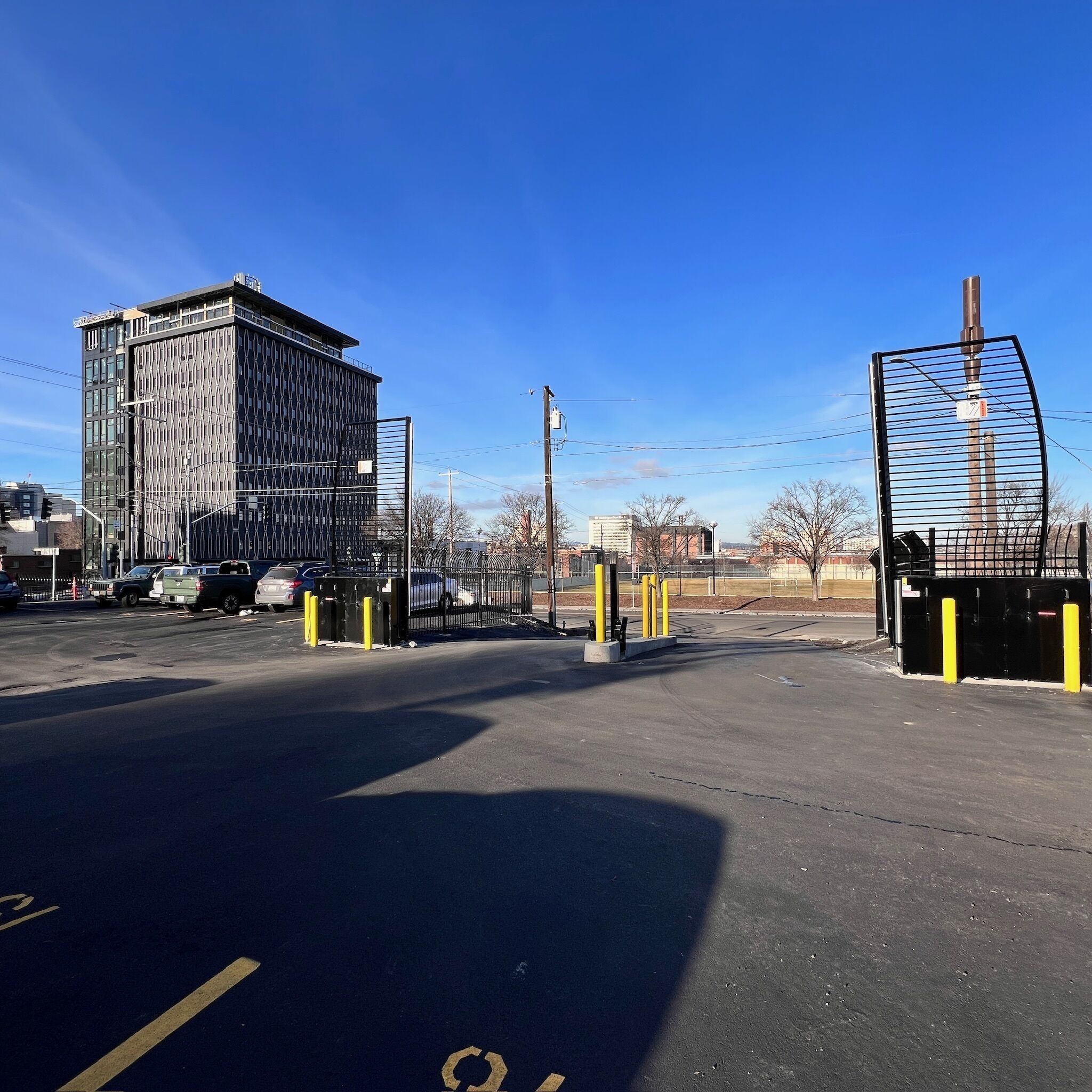 A parking lot with a gated entrance, a tall building with a modern design, and a clear blue sky.