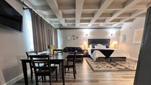 Una habitación de hotel moderna con zona de comedor, una cama con cabecera y un televisor montado en la pared.