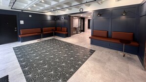 Un moderno vestíbulo con paredes oscuras, alfombra de diseño geométrico y zonas de estar con cojines marrones.