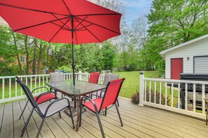 A wooden deck with a table and chairs, a red umbrella, and a barbecue grill. - Boyne City Retreat Near Beaches & Mtn Resort! (Boyne City)