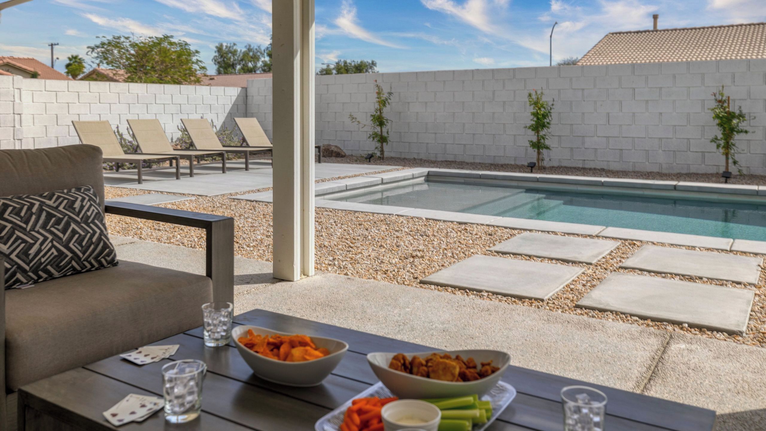 An outdoor pool area with lounge chairs, a dining table with food, and a view of the pool.