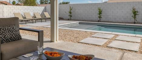 An outdoor pool area with lounge chairs, a dining table with food, and a view of the pool.