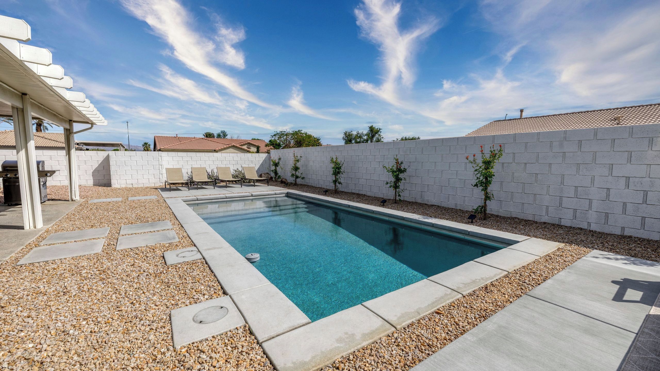 A rectangular swimming pool with a clear blue water, surrounded by a pebble border and a white brick wall.