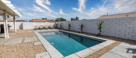 A rectangular swimming pool with a clear blue water, surrounded by a pebble border and a white brick wall.